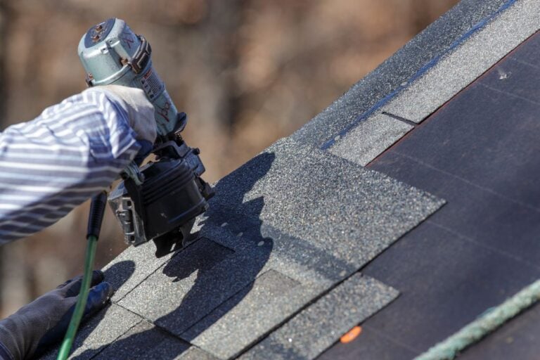 hand attaching shingles to roof