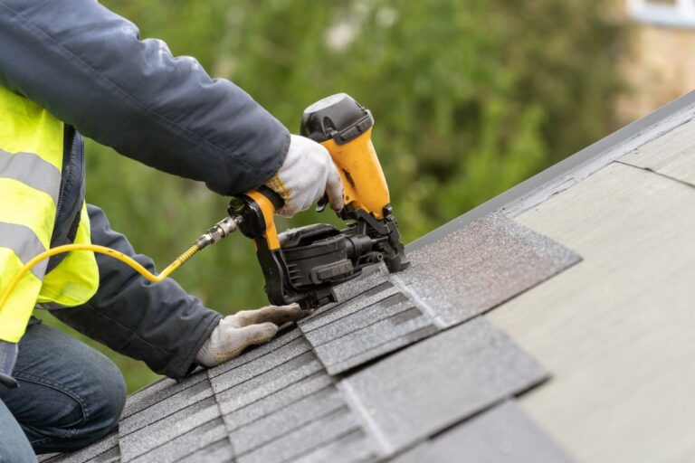 construction worker installing shingles with nail gun