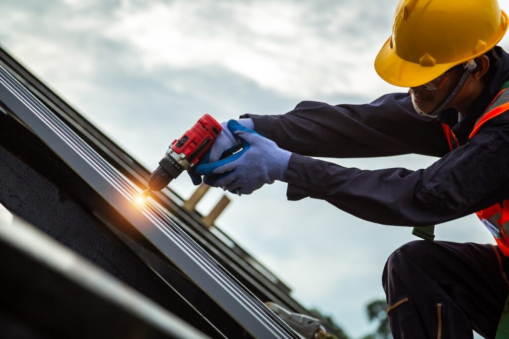 Roofer worker in protective uniform wear and gloves, Construction worker install new roof,Roofing tools,Electric drill used on new roofs with Metal Sheet.