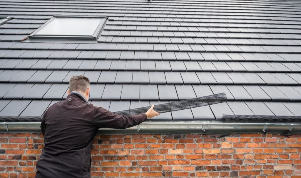 Man puts a gutter mesh to the rain gutter to protect the gutter from leaves