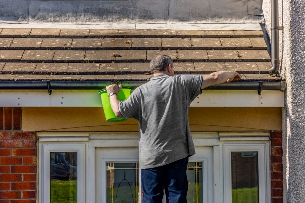 moss on roof man cleaning water gutter