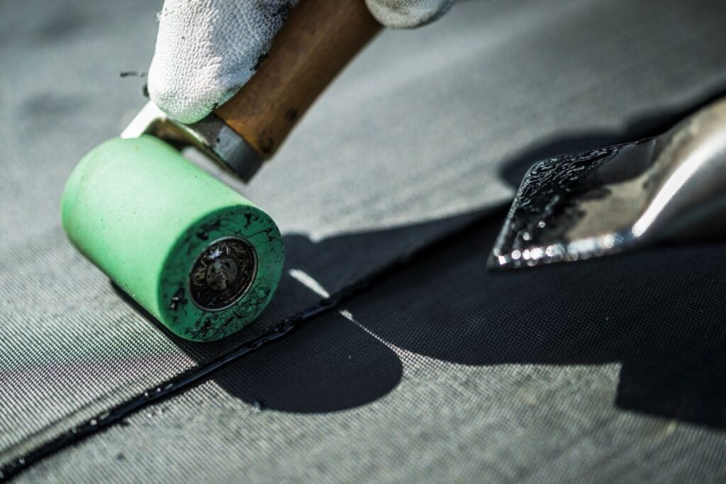 rubber roof repair worker using roller and heat gun
