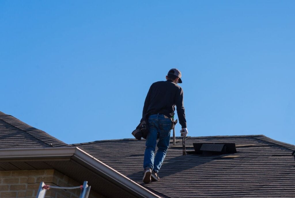 wind damage to roof blue sky worker walking on top of house