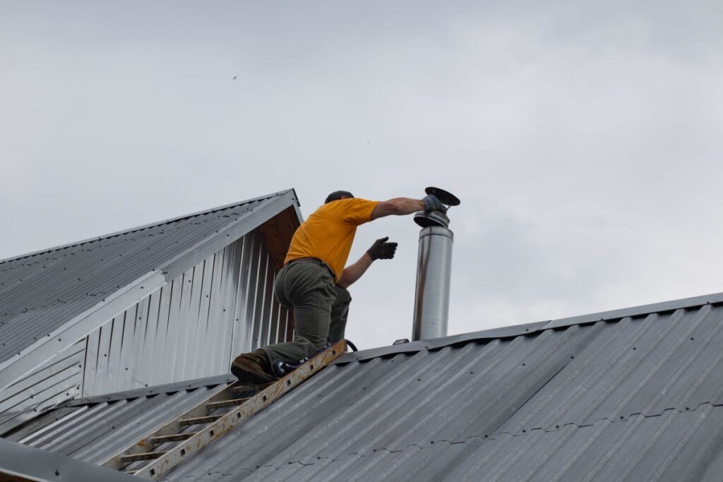 chimney rain cap orange shirt worker replacing unit
