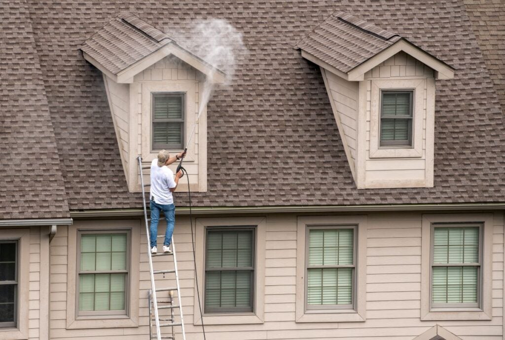 commercial roof cleaning worker using washing gun to clean siding