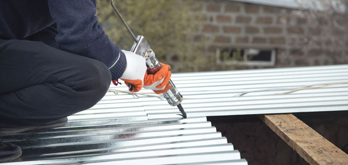 roof sealant worker applying black material on metallic roof