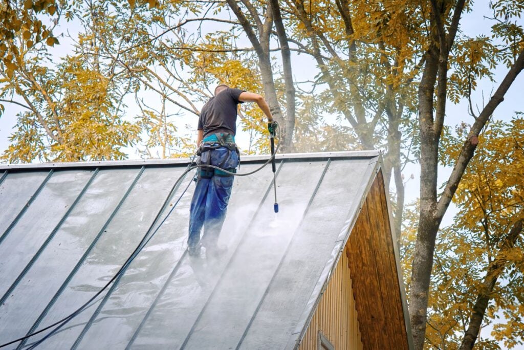 soft wash roof cleaning worker using washing gun on metallic roof