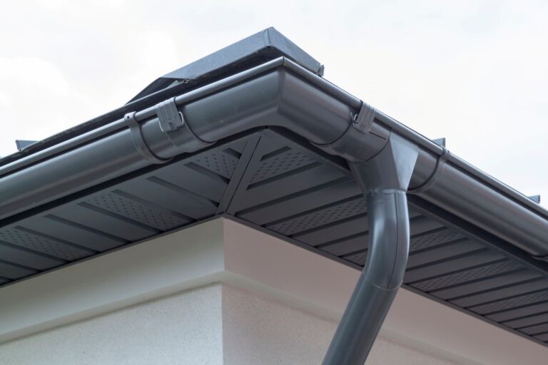 Corner of house with new gray metal tile roof and rain gutter
