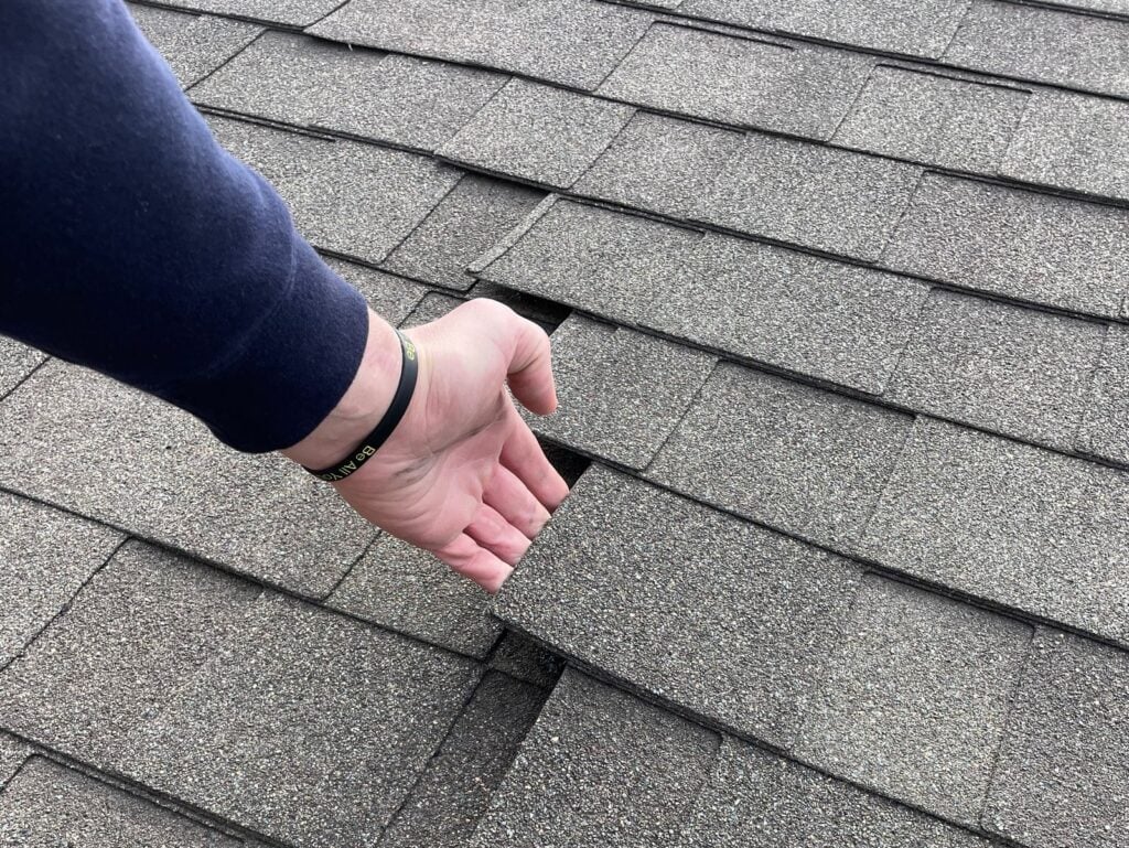 wind damaged shingles hand lifting dark grey shingles