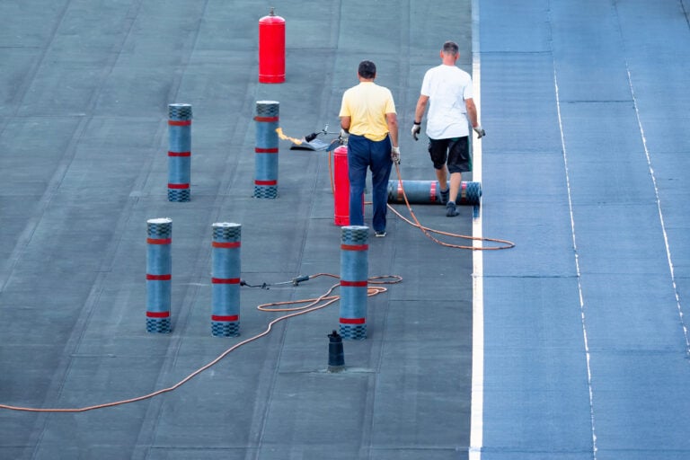 commercial flat roof replacement Roof waterproofing. Two workers are working on installation of waterproofing layer. Man next to rolls of bitumen insulating layer. Roof cover replacement. installation bitumen insulating layer