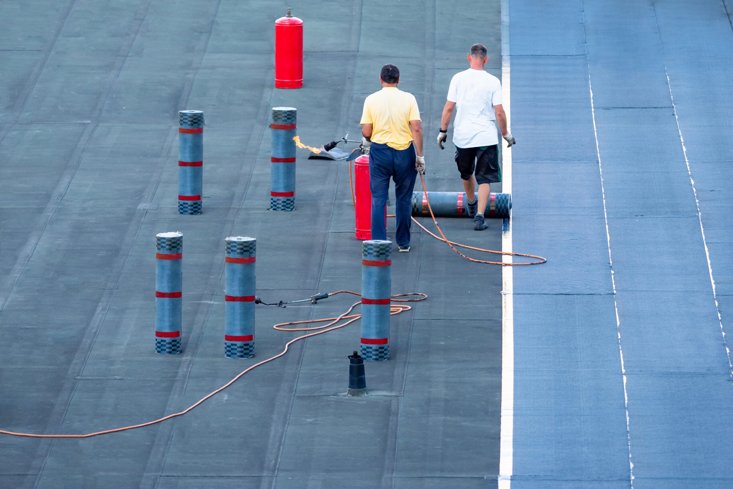commercial flat roof replacement Roof waterproofing. Two workers are working on installation of waterproofing layer. Man next to rolls of bitumen insulating layer. Roof cover replacement. installation bitumen insulating layer