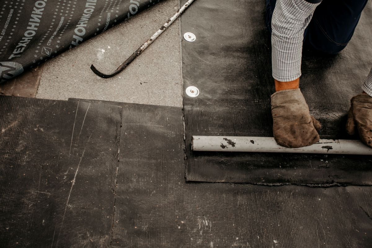 commercial flat roof repair hand holding bitumen roll