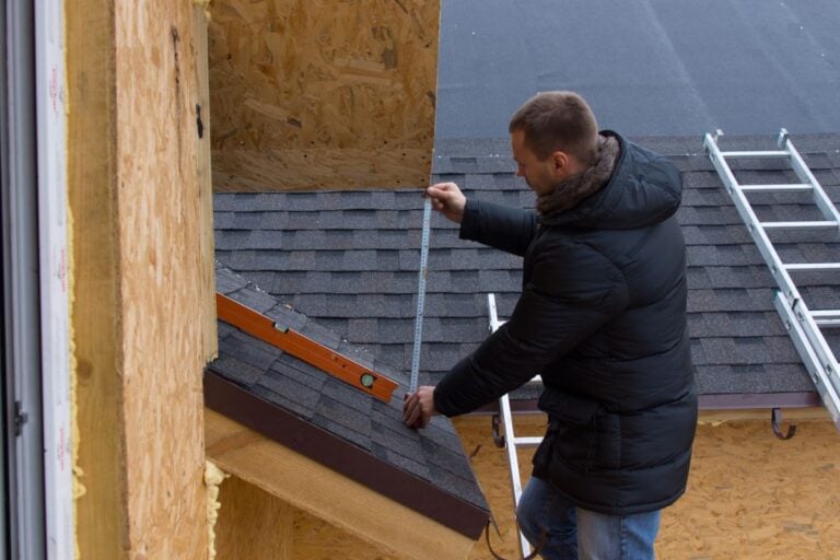 how to calculate roof pitch man holding measure tape on top of shingles roof