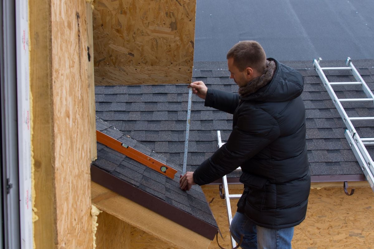 how to calculate roof pitch man holding measure tape on top of shingles roof