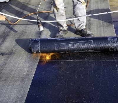 Worker preparing part of bitumen roofing felt roll for melting by gas heater torch flame Worker preparing part of bitumen roofing felt roll for melting by gas heater torch flame; commercial roofing